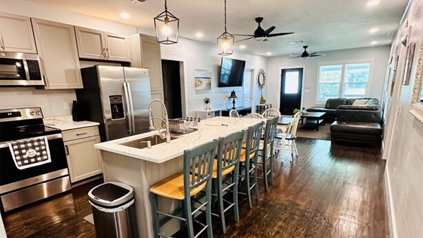 A modern kitchen with stainless steel appliances, a central island with bar stools, and a dining area with a sofa and coffee table. - Renovated Gulf Coast Home - Walk to Marina, Dining, & Downtown Carrabelle (Carrabelle)