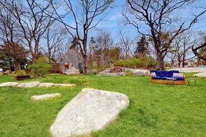 Ein grünes Rasenstück mit einem hölzernen Schuppen, großen Steinen, einem blauen Sofa und einem kleinen Tisch.