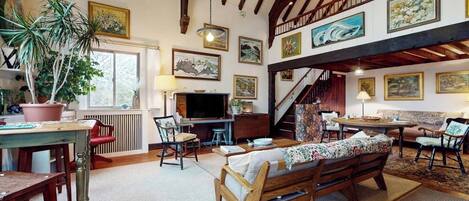 A spacious living area with a wooden bench, a dining table, and a staircase leading to an upper level.