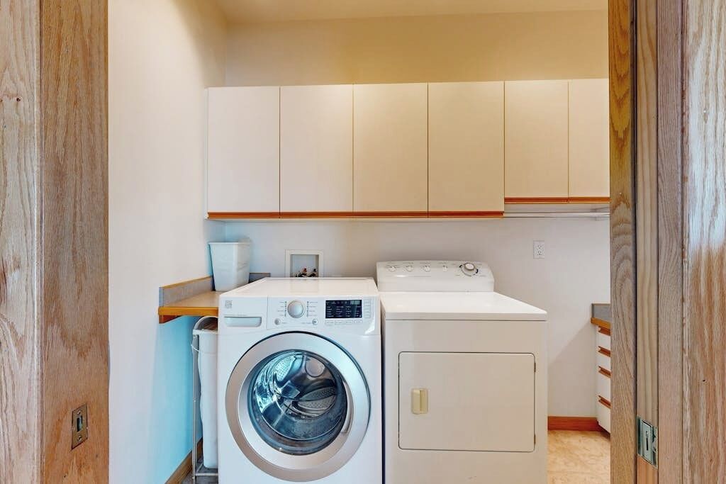 A compact laundry room with a washing machine, dryer, and wooden cabinets.