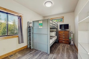 Ein Zimmer mit Etagenbetten, einem Fernseher, einem Schminktisch und einem Fenster mit Vorhängen.