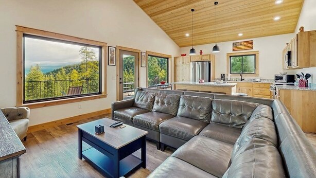 Ein modernes Wohnzimmer mit einer großen Eckcouch, einem Couchtisch und Blick auf einen Wald durch große Fenster.