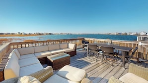 Una terraza con asientos al aire libre, vista al agua y una costa lejana.