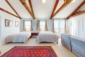 Un dormitorio con dos camas, un tapete rojo estampado y un sofá gris.