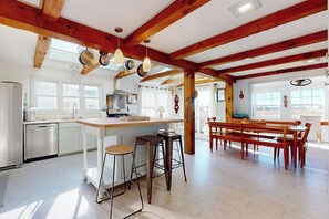 A spacious kitchen with wooden beams, a central island with stools, and a dining area with benches.