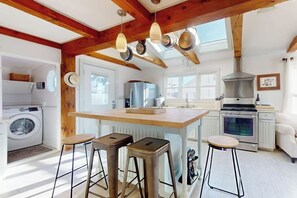Una cocina con una isla central, taburetes de bar, lavadora y un ventanal grande.