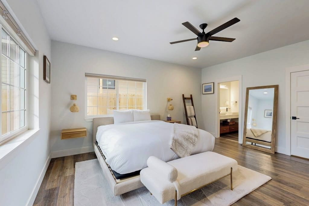 A bedroom with a bed, a bench, a ceiling fan, a window, and a mirror.
