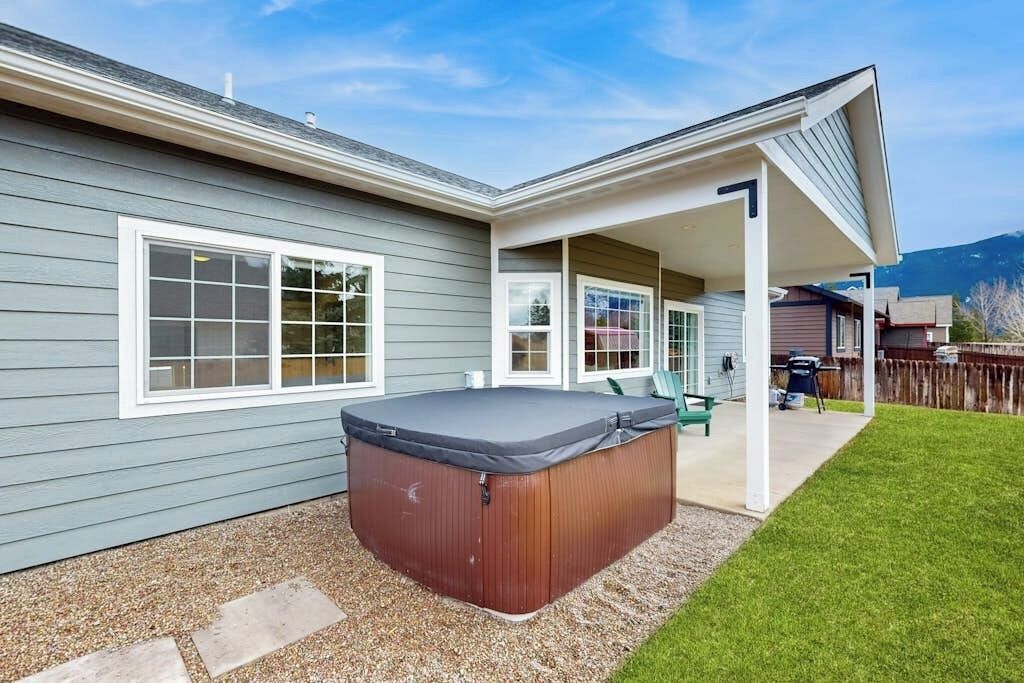A house with a covered patio, a hot tub, and a well-maintained lawn.