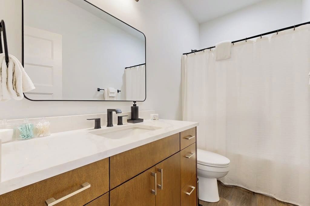 A bathroom with a white sink, a mirror, a toilet, and a shower curtain.