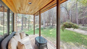 A covered outdoor seating area with a wooden ceiling, a glass table, and a cushioned sofa. - Big Fork rustic loft cabin with forest views, WiFi, 5 miles to Flathead Lake (Bigfork)