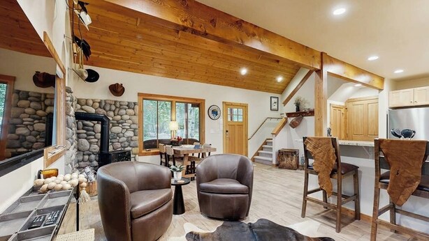 A spacious living area with a stone fireplace, leather chairs, a cowhide rug, and a kitchen with wooden cabinets. - Big Fork rustic loft cabin with forest views, WiFi, 5 miles to Flathead Lake (Bigfork)