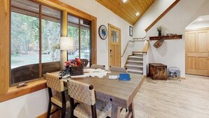 A dining area with a wooden table, chairs, and a window with a view of the outdoors. - Big Fork rustic loft cabin with forest views, WiFi, 5 miles to Flathead Lake (Bigfork)