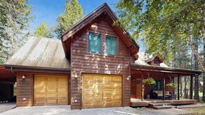 A wooden cabin with two garage doors, a covered porch, and a well-maintained driveway. - Big Fork rustic loft cabin with forest views, WiFi, 5 miles to Flathead Lake (Bigfork)