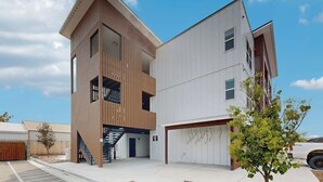 Un edificio moderno de varios pisos con garaje, una escalera y un pequeño árbol al frente.