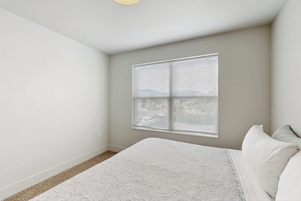 Un dormitorio con cama, ventana con persianas y vista a la ciudad.