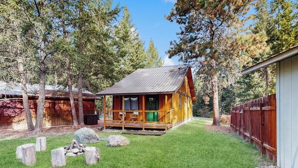 A wooden cabin with a porch, surrounded by trees and a grassy yard. - Charming cabin in Big Fork, pet friendly, firepit, 5 min to Lake, fly-fishing (Bigfork)