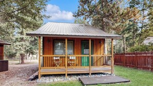 A small wooden cabin with a porch, a green door, and a metal roof. - Charming cabin in Big Fork, pet friendly, firepit, 5 min to Lake, fly-fishing (Bigfork)