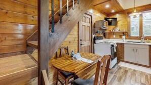A wooden interior with a staircase, a dining table, chairs, a kitchen area, and a television. - Charming cabin in Big Fork, pet friendly, firepit, 5 min to Lake, fly-fishing (Bigfork)