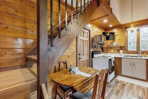A wooden interior with a staircase, a dining table, chairs, a kitchen area with appliances, and a television. - Enjoy two separate cabins, pet friendly, firepit, 5 min to Lake, fly-fishing (Bigfork)