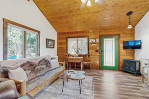 A cozy cabin interior with a wooden ceiling, a sofa, a dining table, and a television. - Enjoy two separate cabins, pet friendly, firepit, 5 min to Lake, fly-fishing (Bigfork)