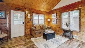 A log cabin interior with a wooden ceiling, a sofa, a coffee table, a door, and a window with blinds. - Enjoy two separate cabins, pet friendly, firepit, 5 min to Lake, fly-fishing (Bigfork)