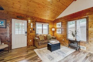 A log cabin interior with a wooden ceiling, a sofa, a coffee table, a door, and a window with blinds. - Enjoy two separate cabins, pet friendly, firepit, 5 min to Lake, fly-fishing (Bigfork)
