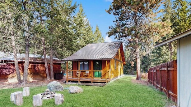 A cabin with a porch, surrounded by a grassy yard and trees. - Enjoy two separate cabins, pet friendly, firepit, 5 min to Lake, fly-fishing (Bigfork)