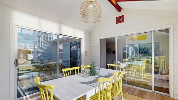 A dining area with a white table and yellow chairs, large glass sliding doors, and a woven light fixture. - Inviting coastal home w/ yard:  walk to beach, town & train (Rockport)