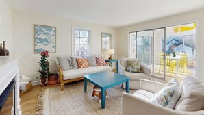 A living room with a sofa, a coffee table, and a chair. There are two windows and a view of the outside. - Inviting coastal home w/ yard:  walk to beach, town & train (Rockport)