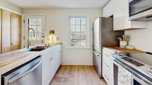 A kitchen with white cabinets, a stainless steel refrigerator, a window, and a wooden floor. - Inviting coastal home w/ yard:  walk to beach, town & train (Rockport)