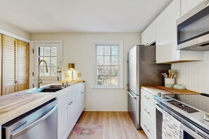 A kitchen with white cabinets, a stainless steel refrigerator, a window, and a wooden floor.