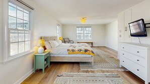 A bedroom with a bed, bedside table, lamp, TV, and a view of the city. - Inviting coastal home w/ yard:  walk to beach, town & train (Rockport)