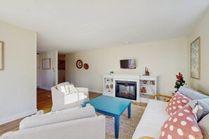 A living room with a fireplace, white sofas, a blue coffee table, and a TV mounted above the fireplace.