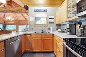 A modern kitchen with wooden cabinets, a stainless steel dishwasher, and a built-in oven. - Dog-Friendly Home with Free WiFi, Private Hot Tub, and Great Views - Near Golfing (Big Sky)