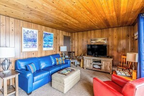 Ein Zimmer mit Holzwandverkleidung, einem blauen Ledersofa, einem roten Sofa, einem Fernseher und gerahmten Bildern an der Wand.