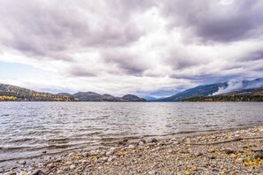 Ein See mit steinigem Ufer, umgeben von Bergen und Bäumen.