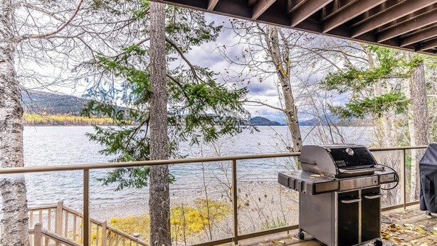 En terrass med grillplats, med utsikt över en sjö omgiven av träd och berg.