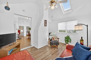 Een moderne woonkamer met een televisie, een rode bank, een gestreept fauteuil en een plafondventilator.