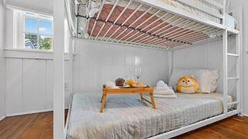 A bunk bed room with a wooden tray table, a plush toy, and a window with a view of trees.