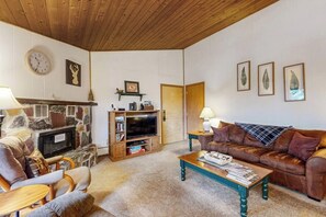 A cozy living room with a stone fireplace, wooden ceiling, and a brown leather sofa.