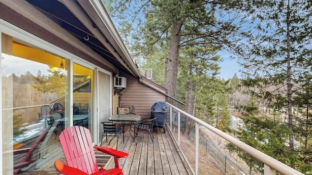 A wooden deck with outdoor furniture, a glass door leading inside, and a view of trees. - Dog-friendly condo with lake view, hot tub & pool - near beach access (Whitefish)
