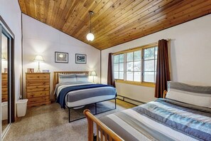 A bedroom with a wooden ceiling, two beds, a window, and a mirror.