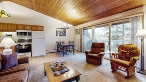 A cozy living room with a wooden ceiling, a dining area with a table and chairs, and a kitchen with appliances. - Dog-friendly condo with lake view, hot tub & pool - near beach access (Whitefish)