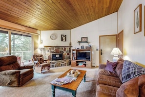 A cozy living room with a stone fireplace, comfortable seating, a television, and a bookshelf.