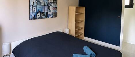 A bedroom with a large bed, a wall-mounted light fixture, a bookshelf, and a poster on the wall.