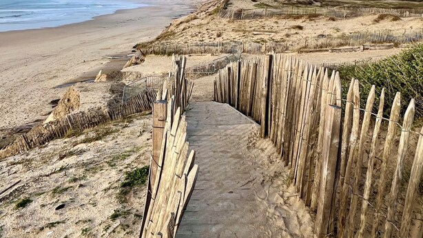 Un vialetto in cemento conduce a una spiaggia, delimitato da recinzioni in legno.