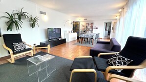 Un soggiorno moderno con una TV a schermo piatto, un'area pranzo con tavolo e sedie, e una cucina sullo sfondo.