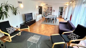 A living room with a TV, sofa, chairs, and a dining area.