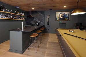 A bar area with a pool table, stools, and a variety of liquor bottles on shelves.