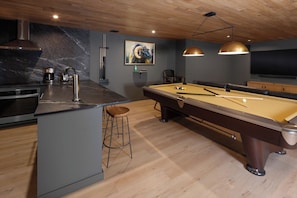 A modern kitchen with a built-in stove, a coffee machine, and a pool table.